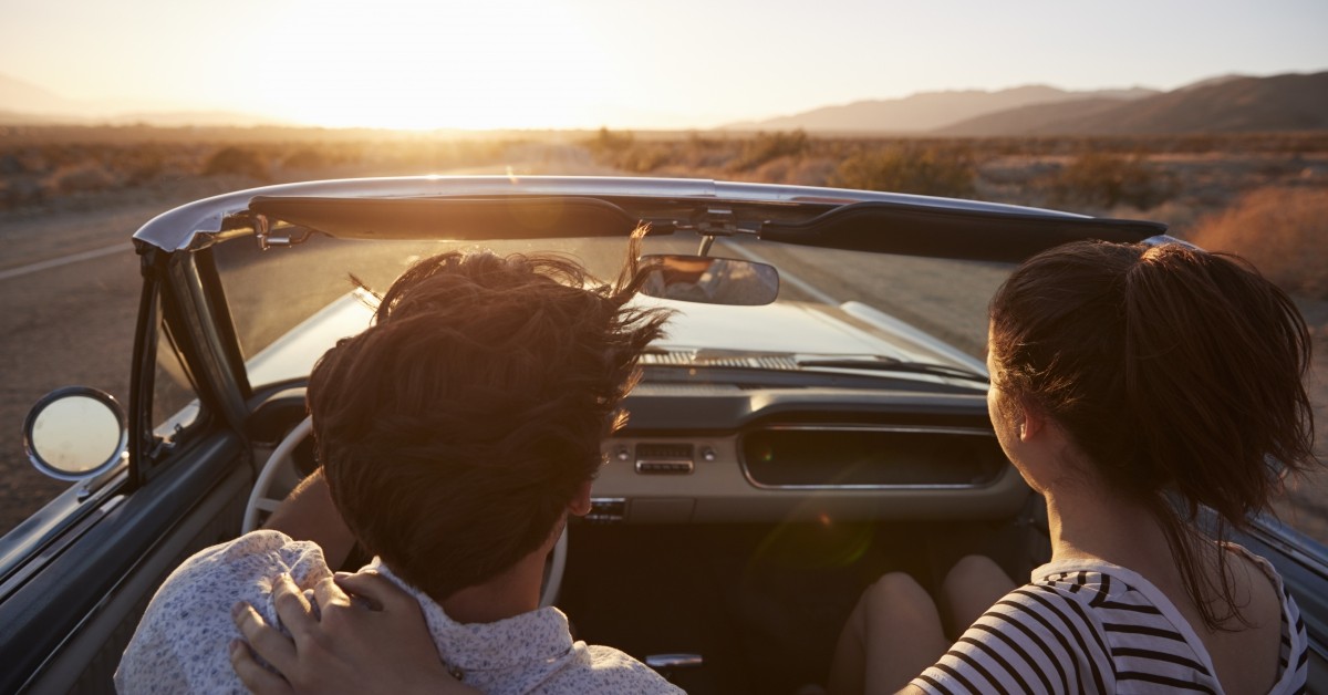 Over-the-shoulder view of man and woman in convertible driving in the desert
