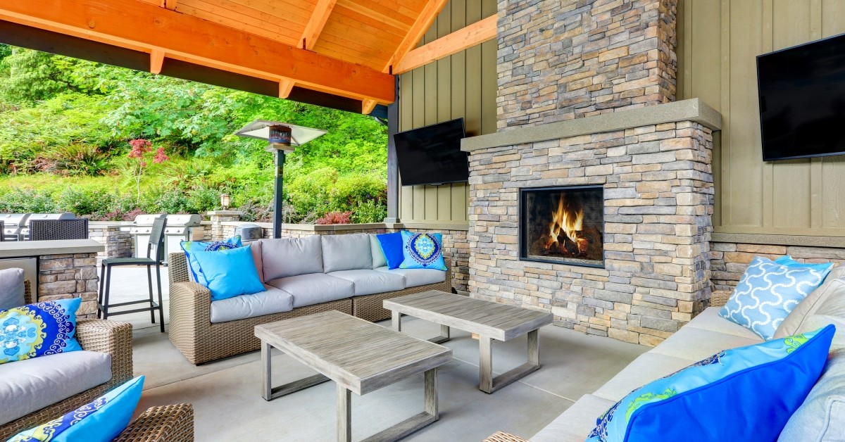 Wicker outdoor patio lounge furniture with blue pillows arranged around outdoor fire place