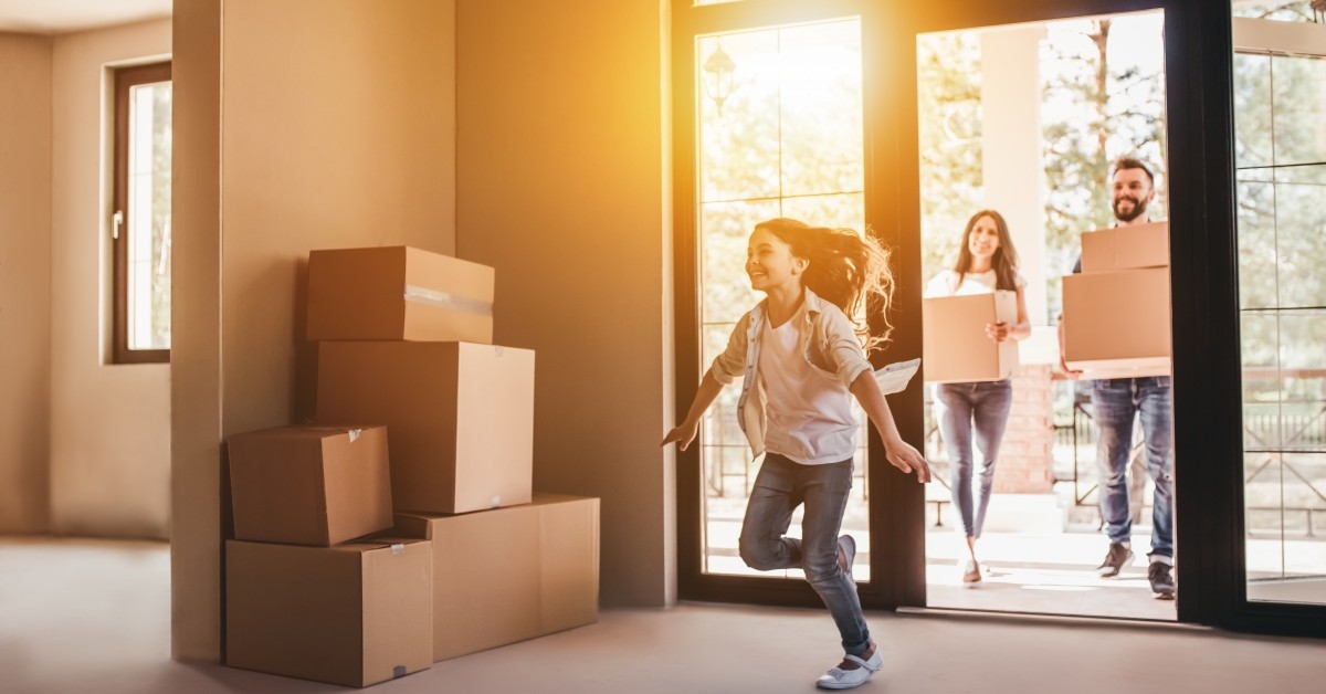 Young girl running into new home with parents carrying in moving boxes