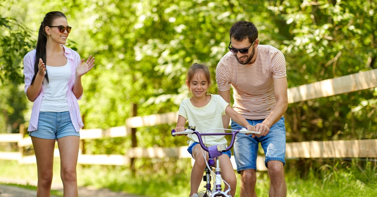 Two parents teaching their daughter to ride a bike