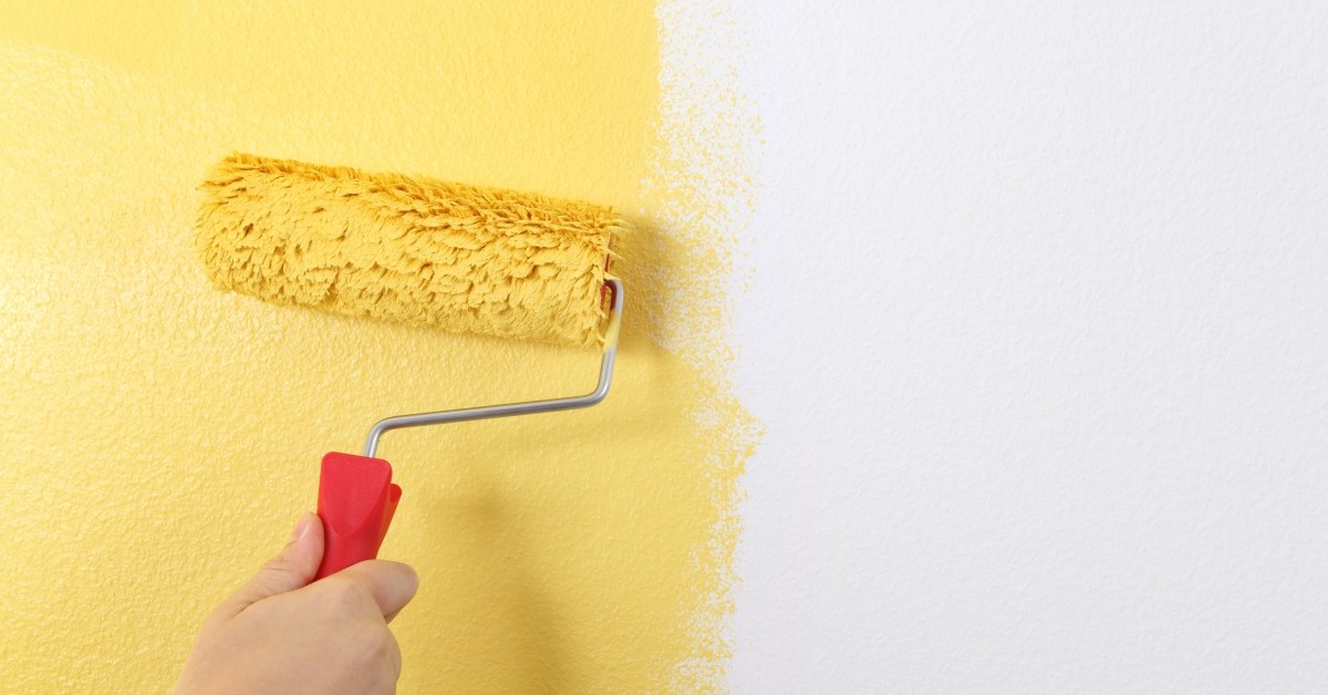 Close up of paint roller against a wall with fresh, yellow paint