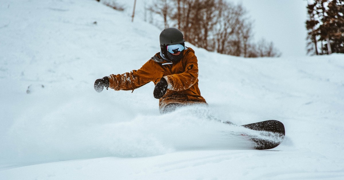 Person on snow board with helmet, gloves and goggles spraying up snow as he turns.