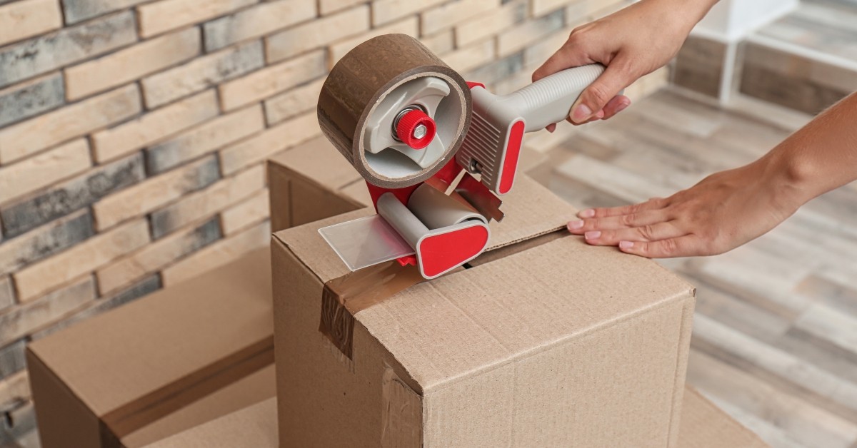 Close-up of hands using packing tape to seal a cardboard box.
