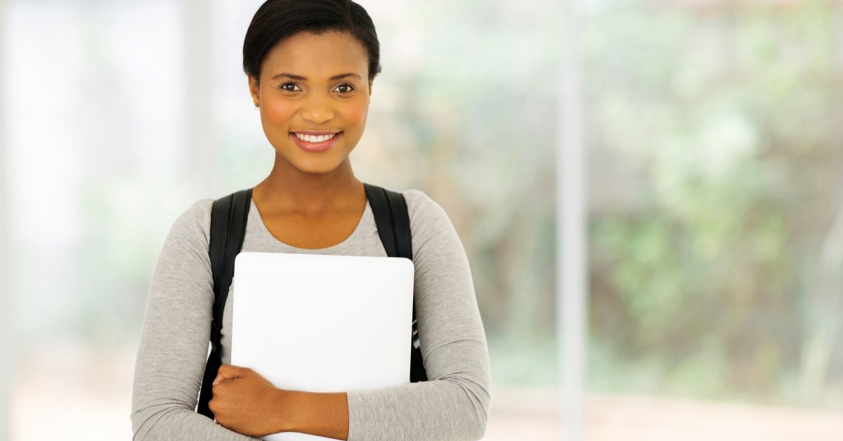College-aged woman smiling, holding a laptop and wearing a backpack.