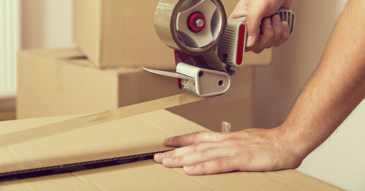 Close-up of hands using packing tape to seal a cardboard box.