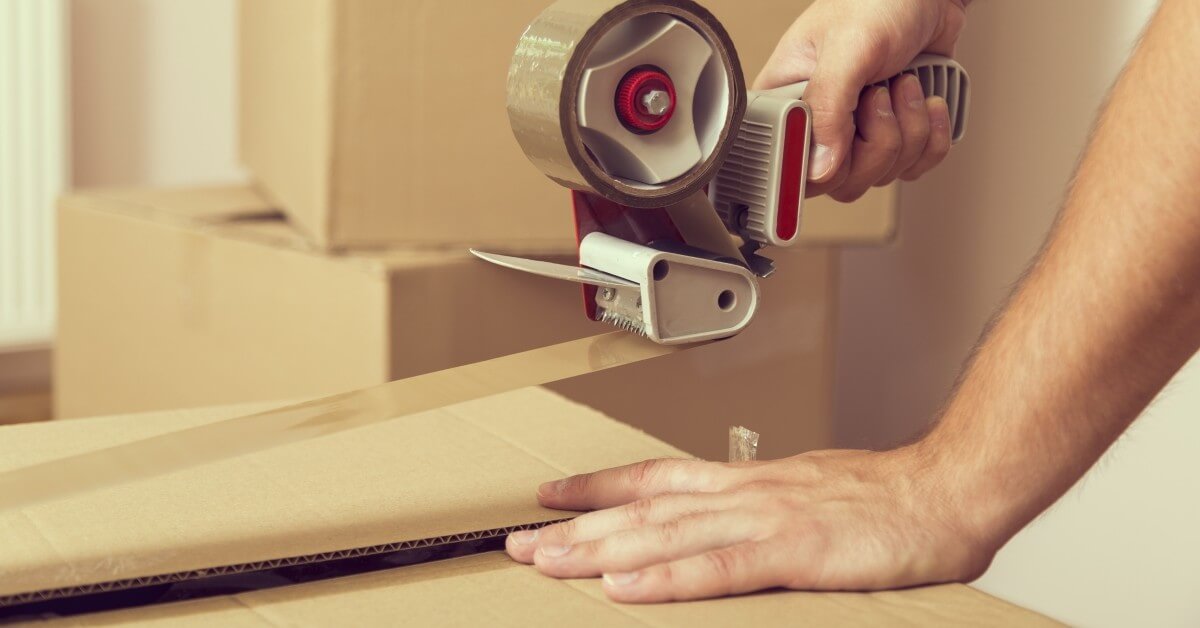 Close-up of hands using packing tape to seal a cardboard box.
