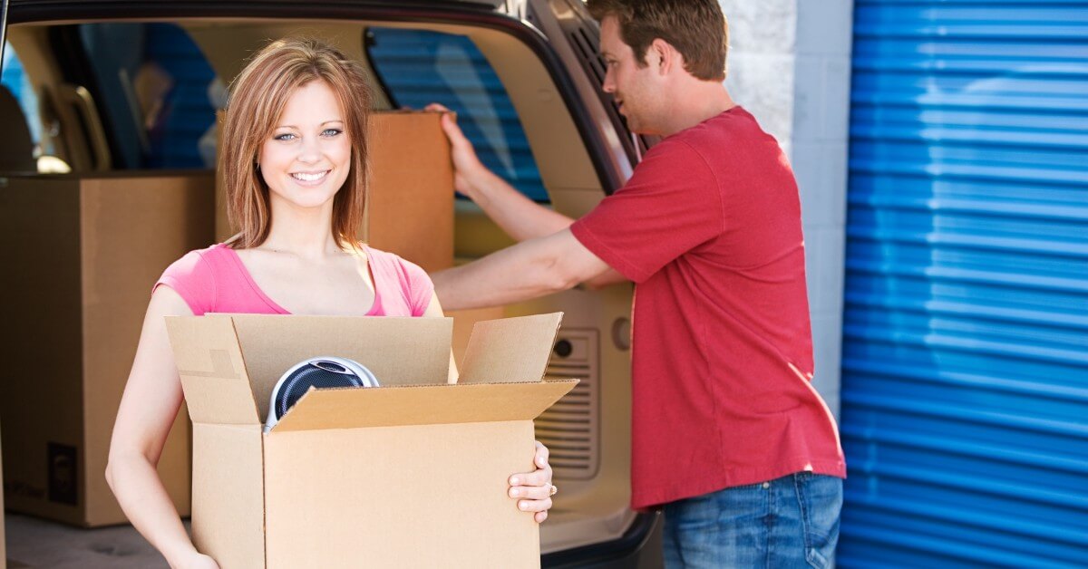 Man and woman unloading boxes from SUV with storage unit in background.