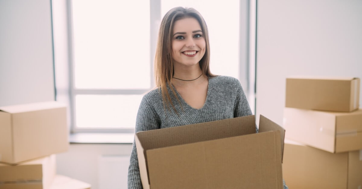 Smiling woman in gray sweater packing items into box