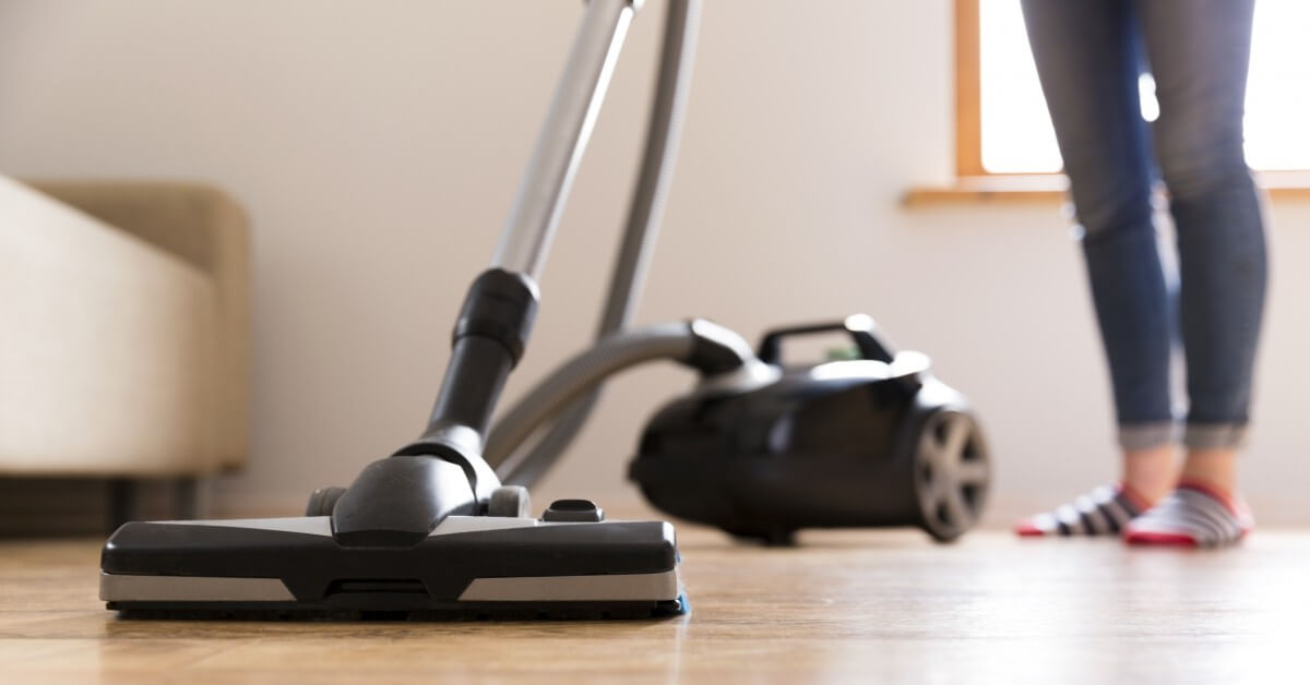 Close up of woman's feet standing next to vaccuum cleaner in living room.