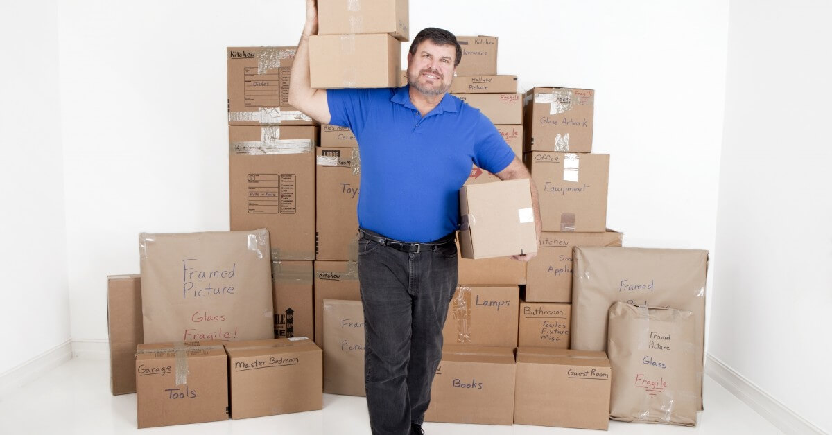 Man carrying a moving box in white room full of moving boxes.