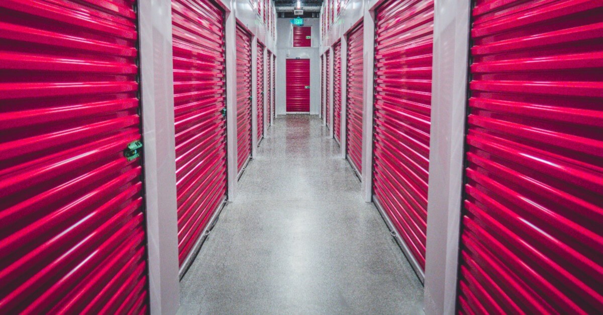 View of storage facility hallway with red shuttered doors on either side.