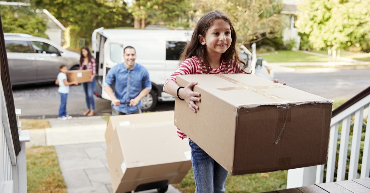 Mother, father with young son and daughter moving boxes from van to the front steps of a house.