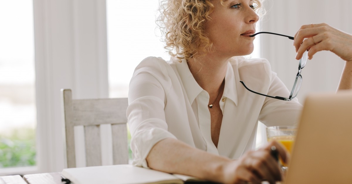 Woman with glasses at laptop thinking