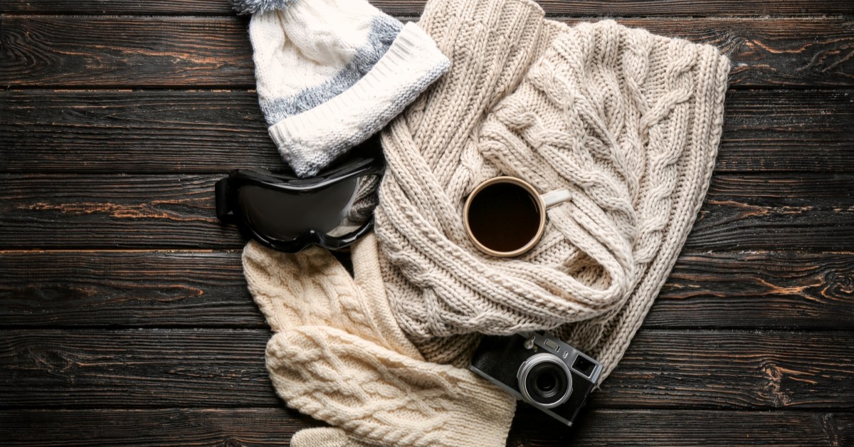 Wooden table with sweater, wool hat, ski goggles, coffee, and camera