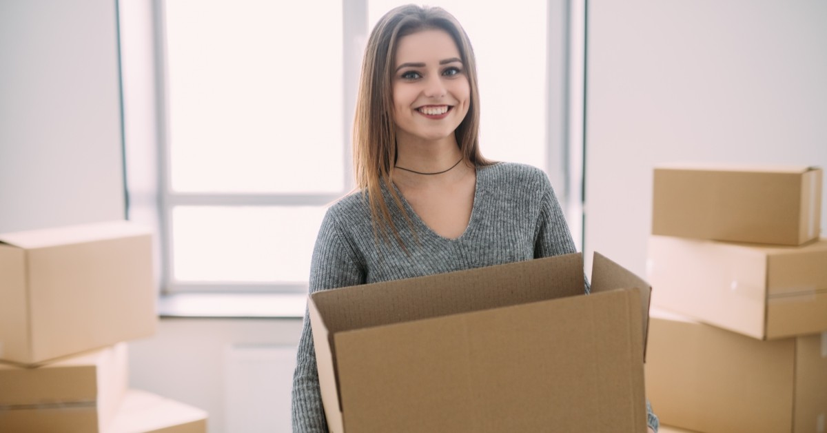 Smiling woman in gray sweater holding moving box