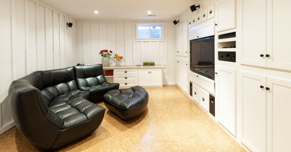 Finished basement with black sectional couch and white walls and cabinets